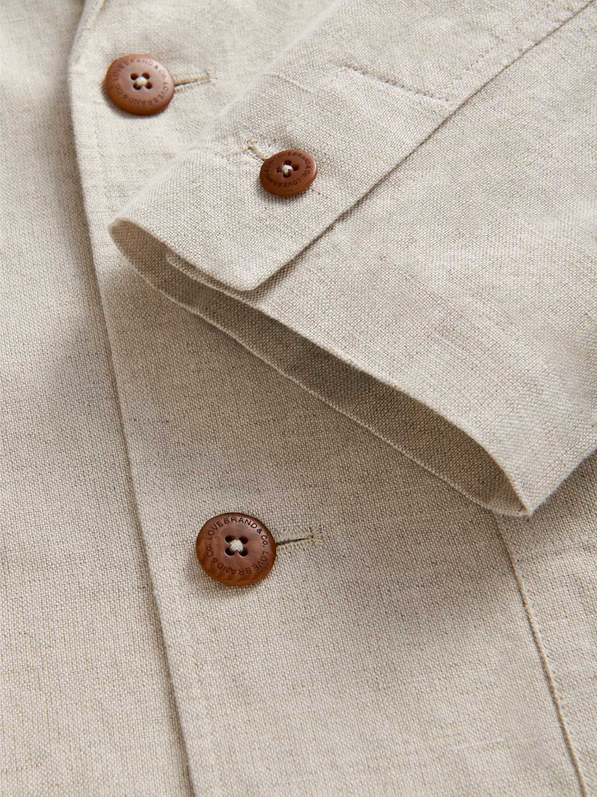 Close-up of an ecru coloured linen jacket with brown buttons