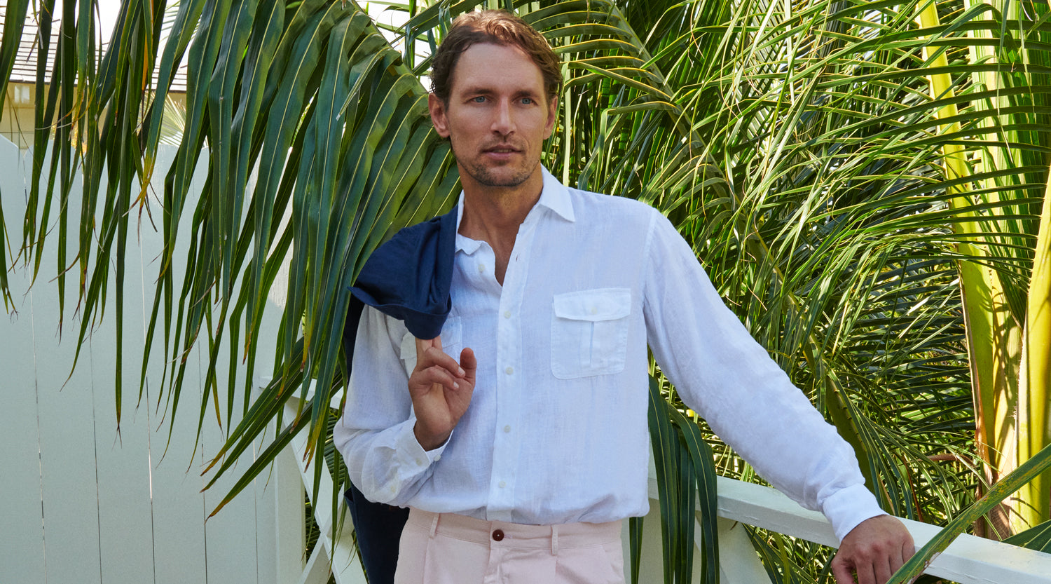 Man holding a blue linen jacket against a tropical background with palm leaves