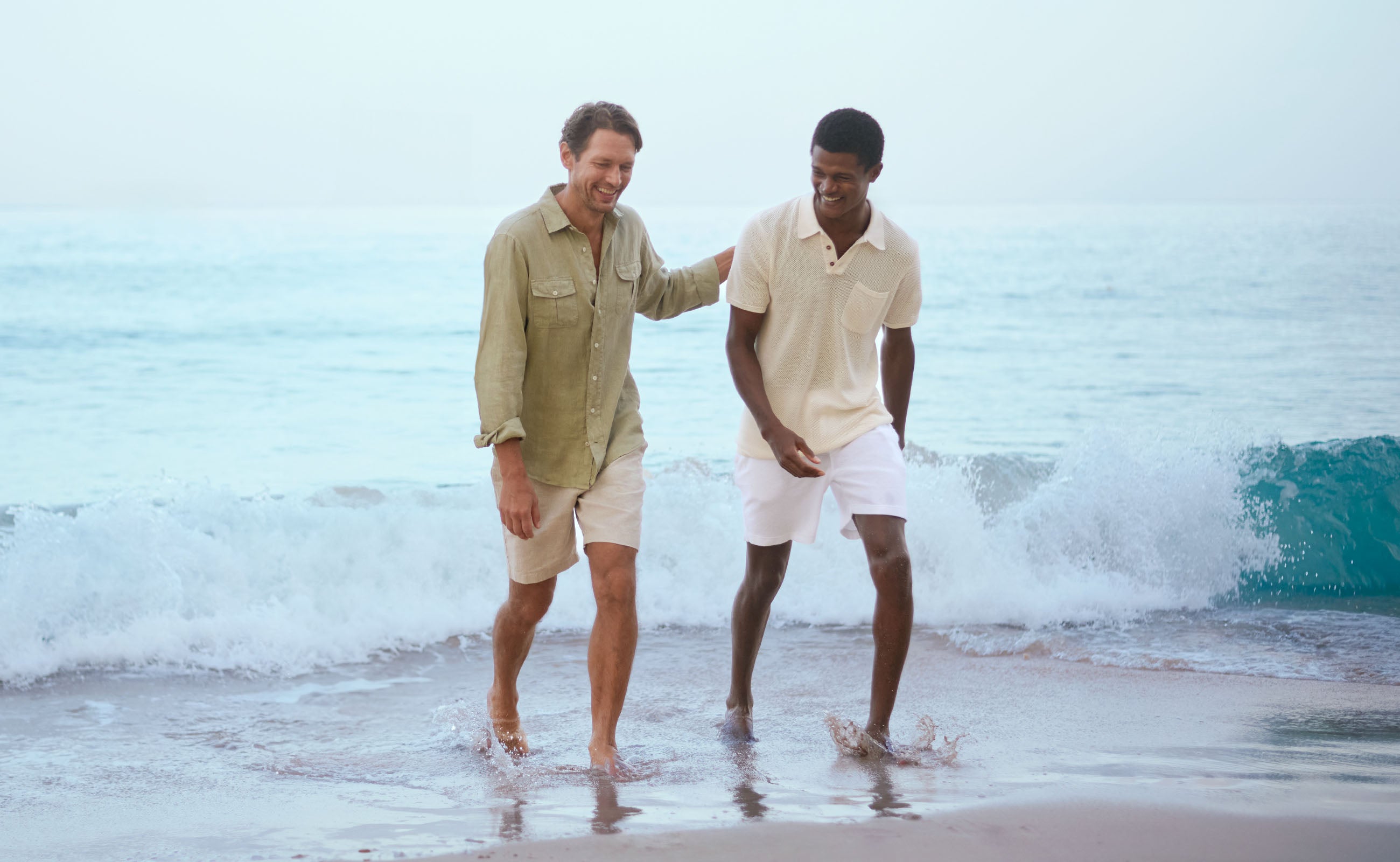 Two men walking on a beach with ocean waves in the background wearing love brand resort wear