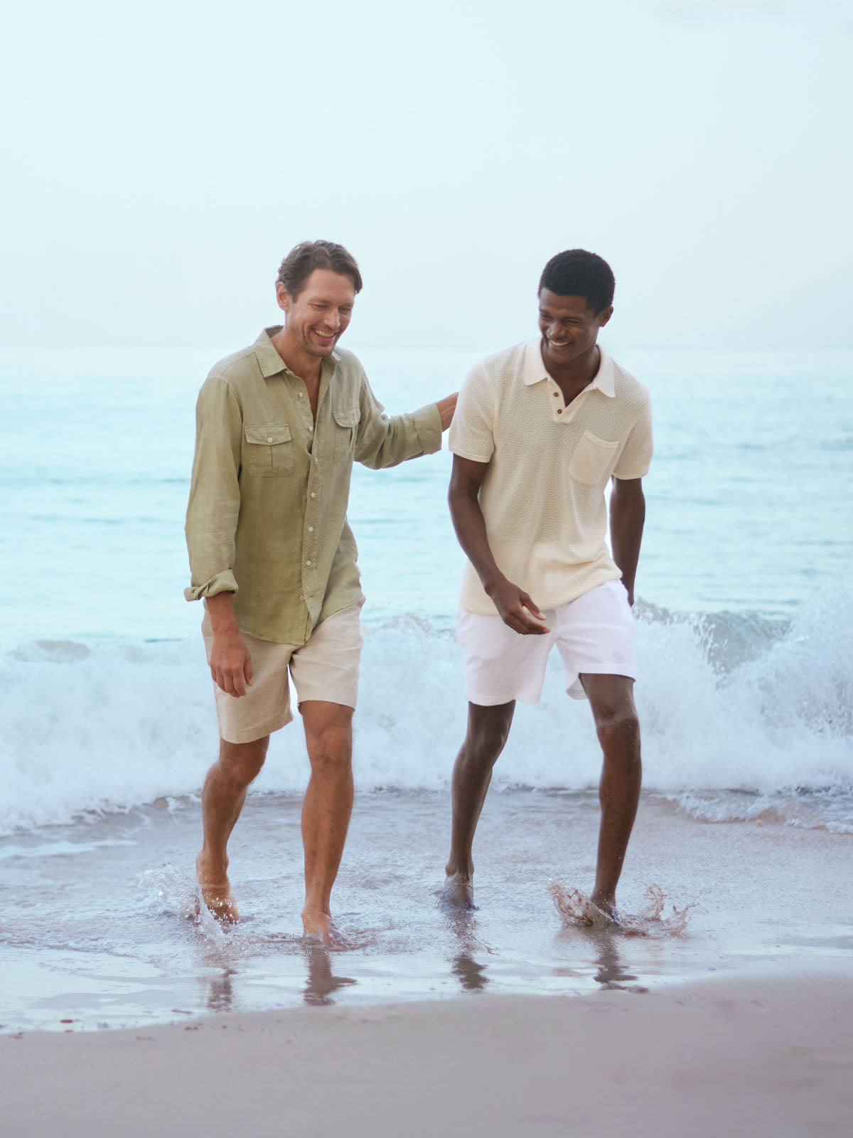 Two men walking on a beach with ocean waves in the background wearing resort wear