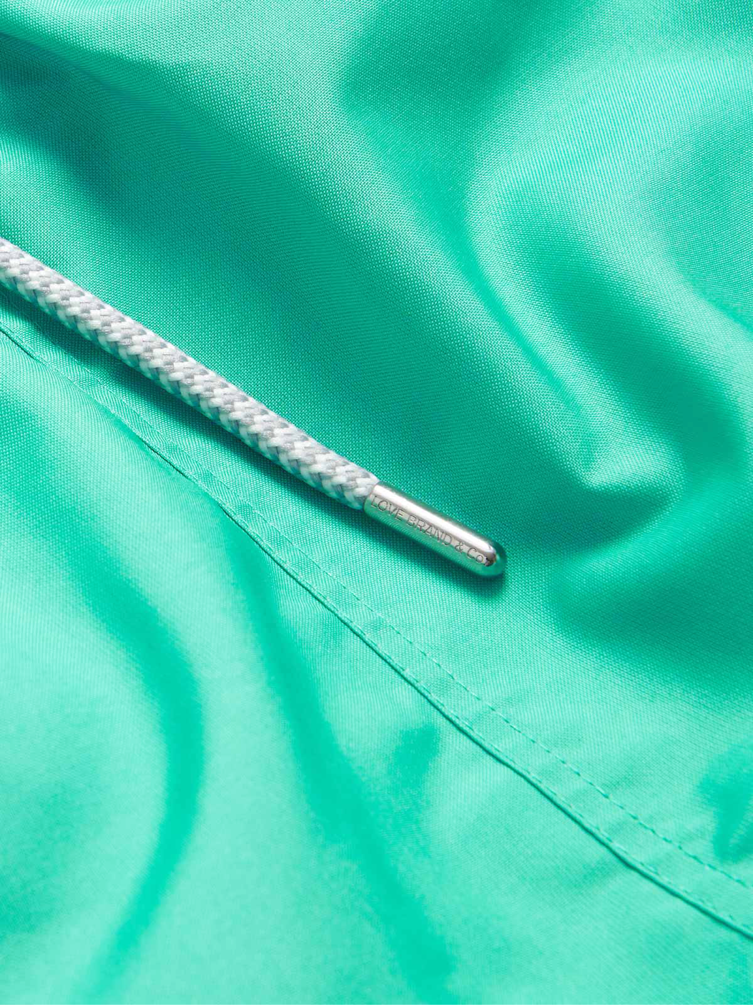Close-up of a bright turquoise-green fabric surface with a white braided drawstring threaded through a metal eyelet.