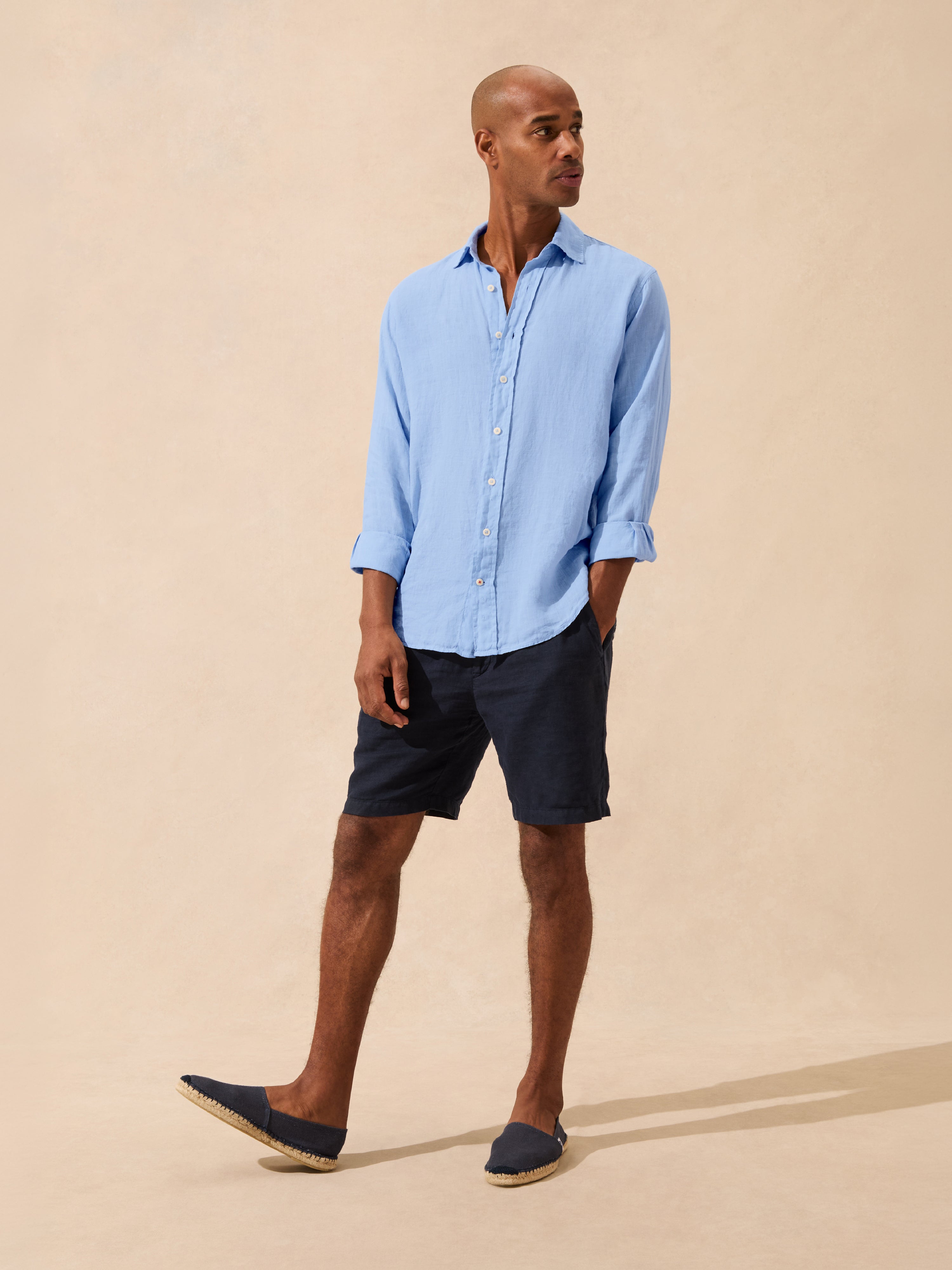 Man wearing a light blue shirt and dark shorts on a beige background
