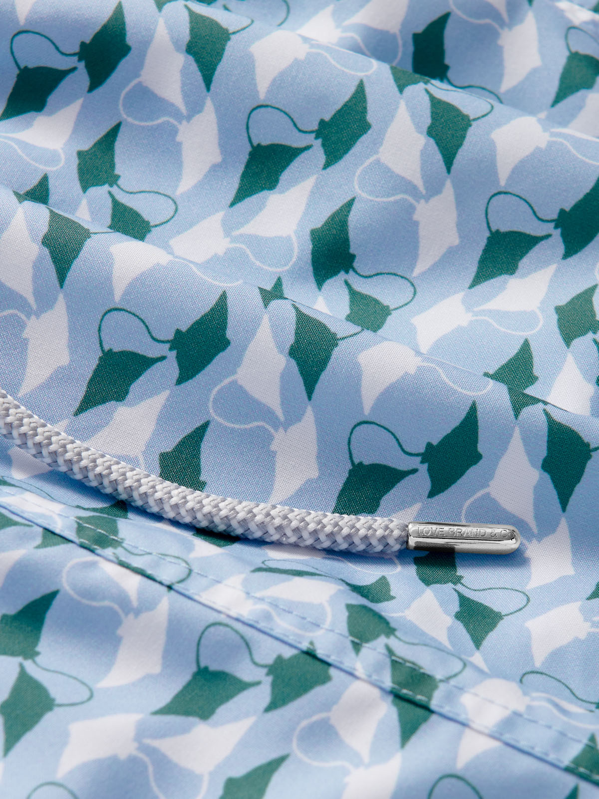 Close-up of the patterned fabric detail on the "Men's Which Way to the Tropics Staniel Swim Shorts," featuring an emerald and white manta ray design, with a white drawstring.