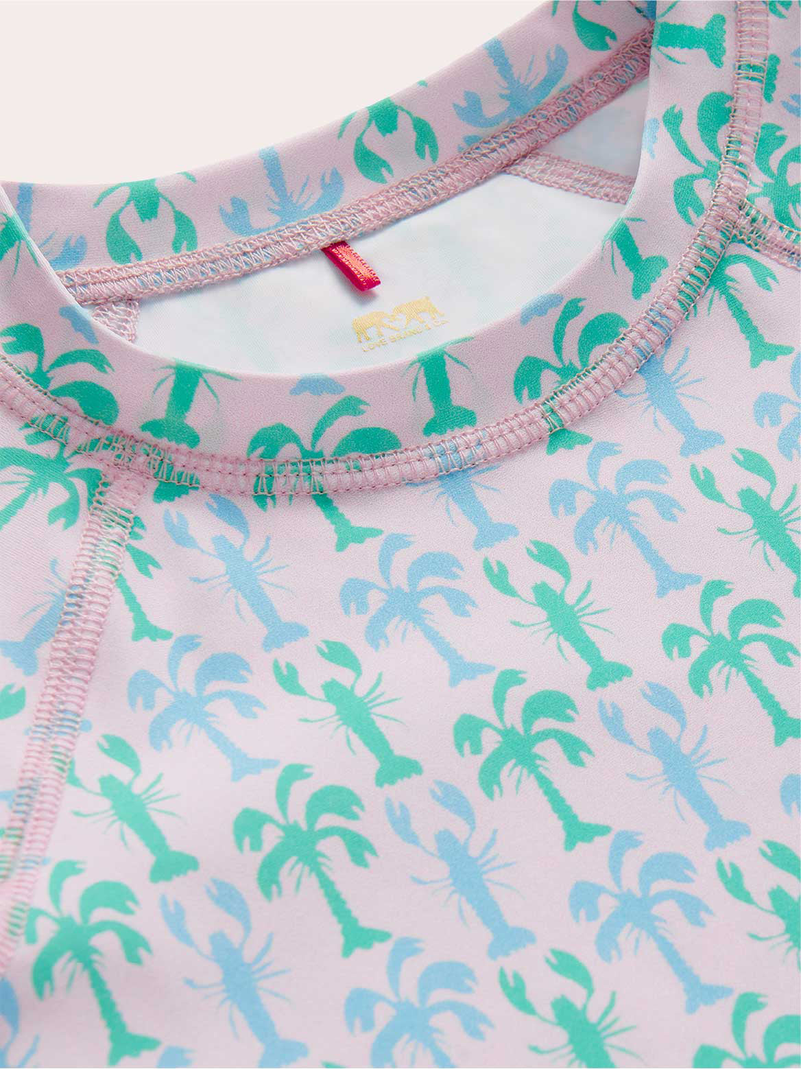 close-up of pink kids rash vest with lobster and palm tree pattern.