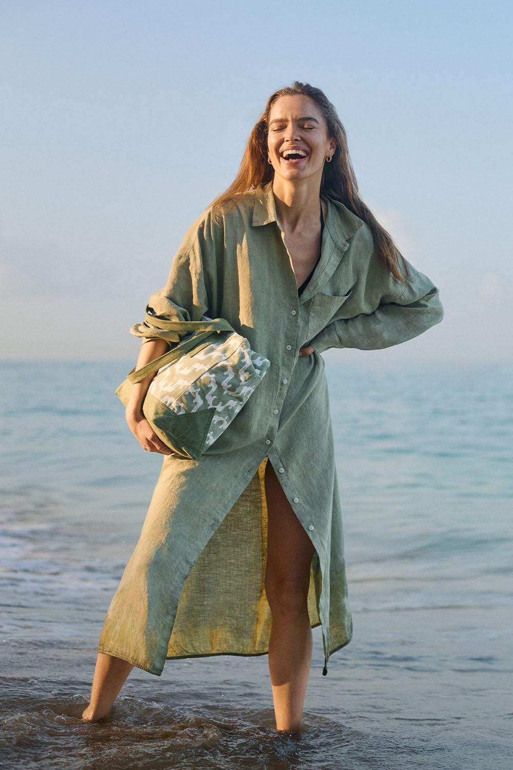 woman wears long women's resort apparel dress standing in ocean.