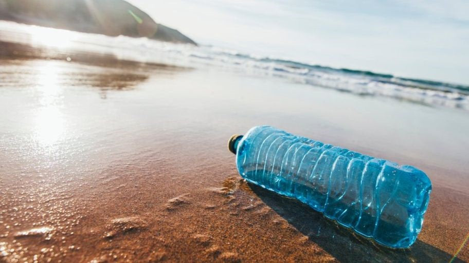 Blue water bottle on a beach with waves in the background