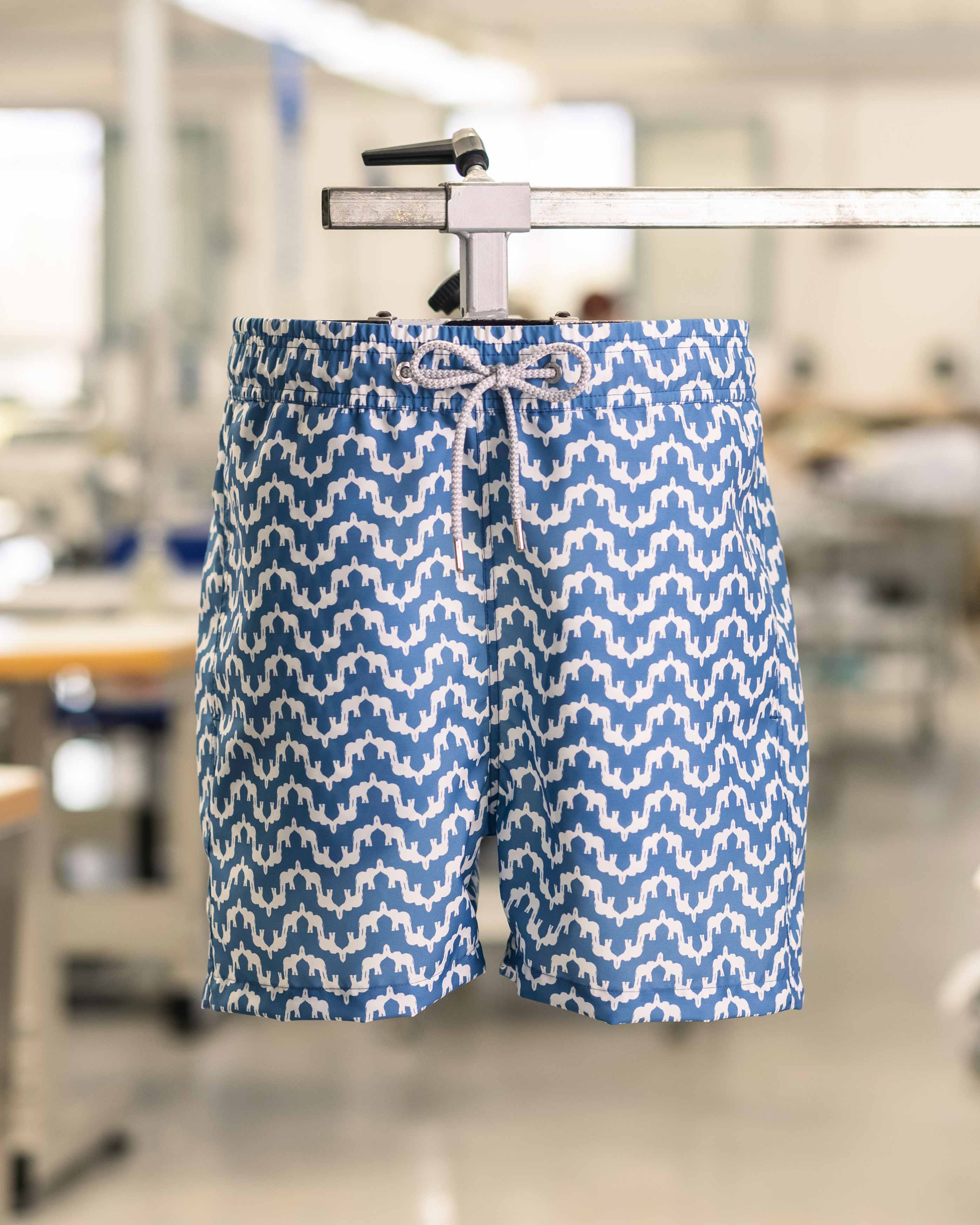 Blue and white patterned swim shorts on a hanger with a blurred indoor background