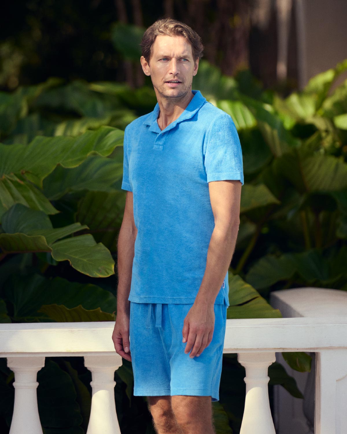 Man wearing a blue terry towelling outfit standing in front of green foliage