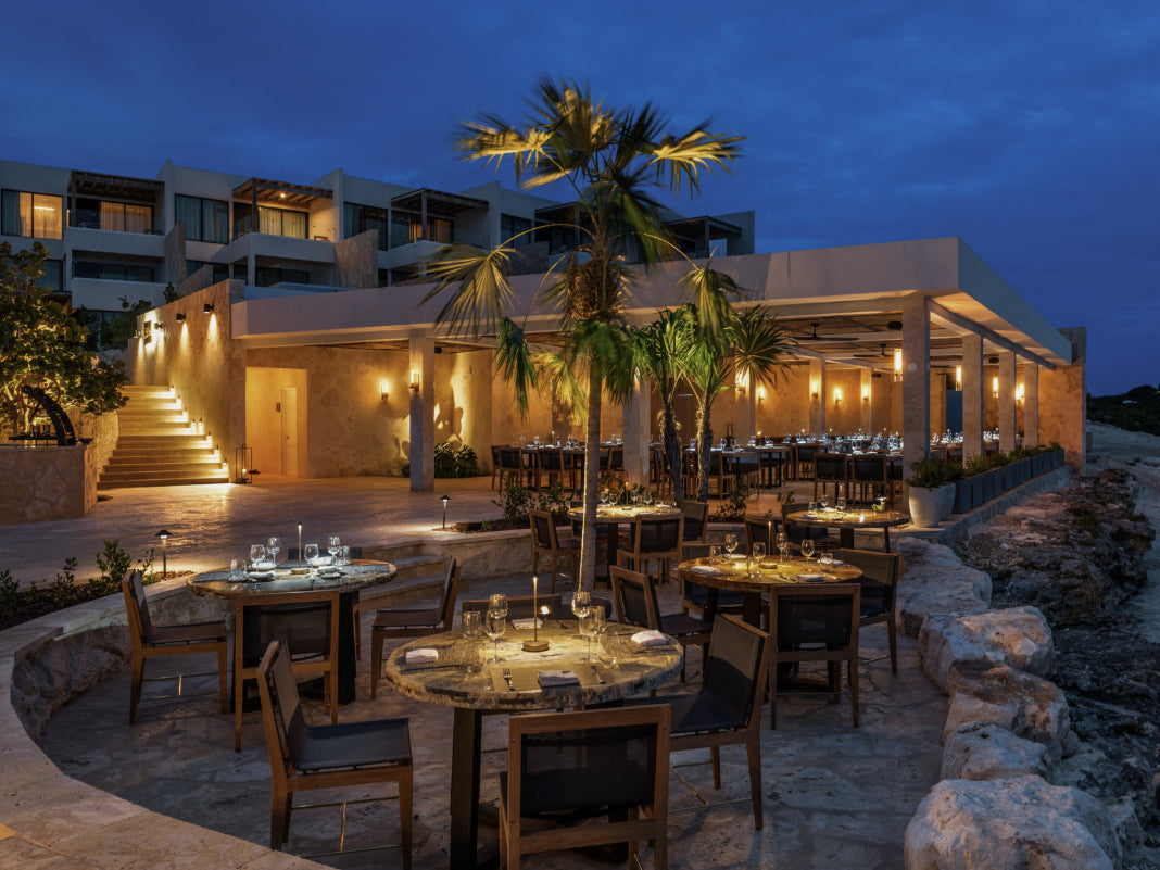 Outdoor dining area in Turks & Caicos with tables and chairs in front of a building at dusk.