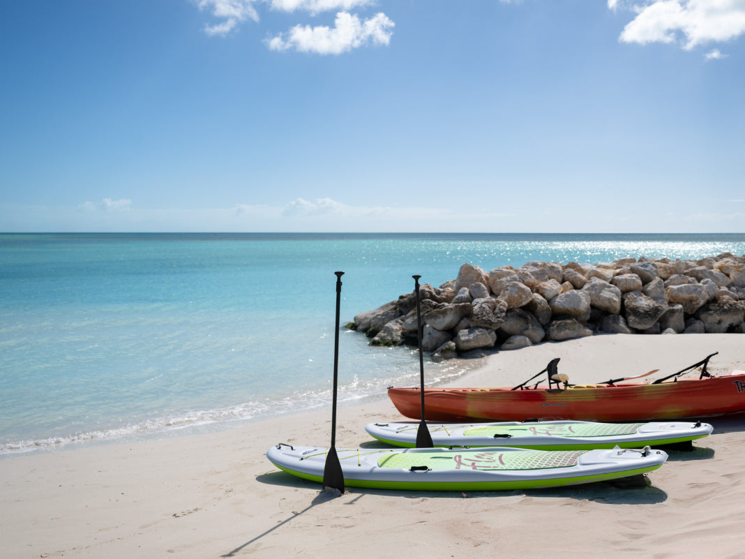 Kayaks on a sandy beach in turks and caicos with clear blue water and a rocky breakwater in the background.