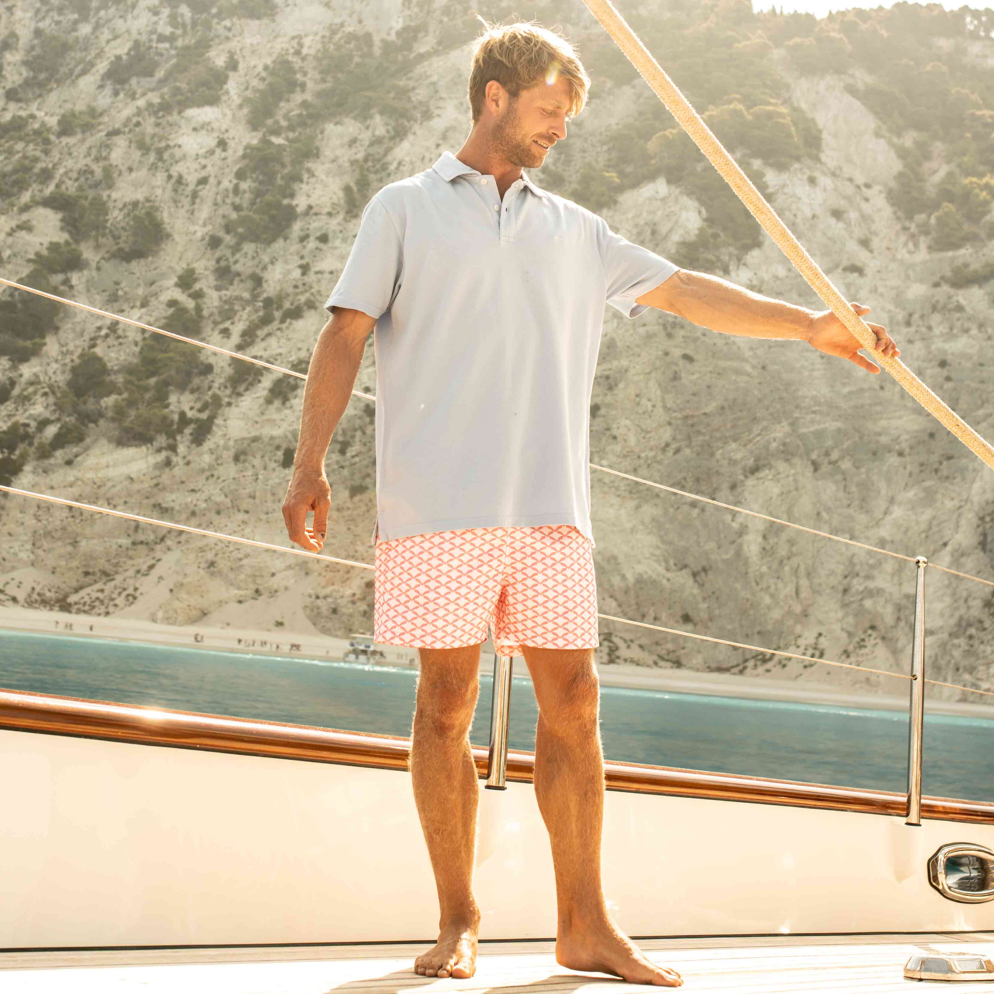 beachwear to wear on a yacht featuring blue cotton polo shirt and patterned red swim shorts