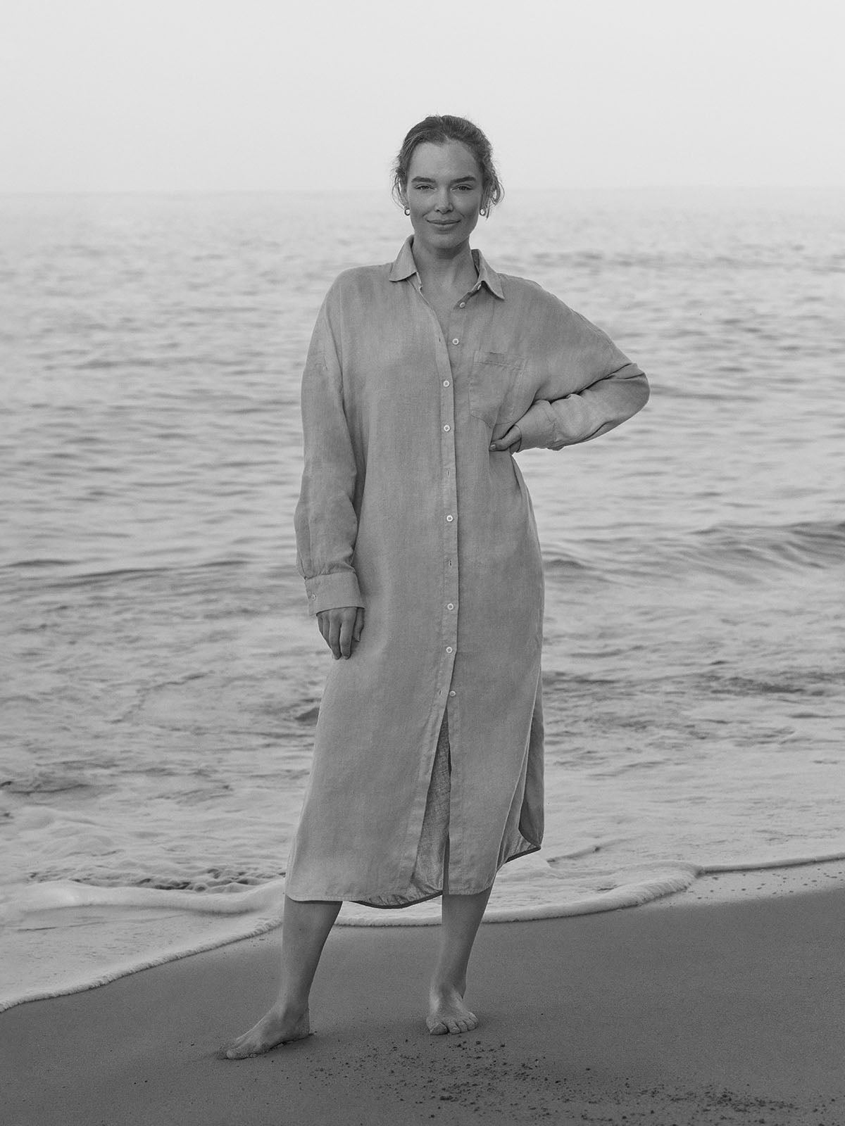 Person wearing a long beige dress standing on a beach with ocean waves in the background