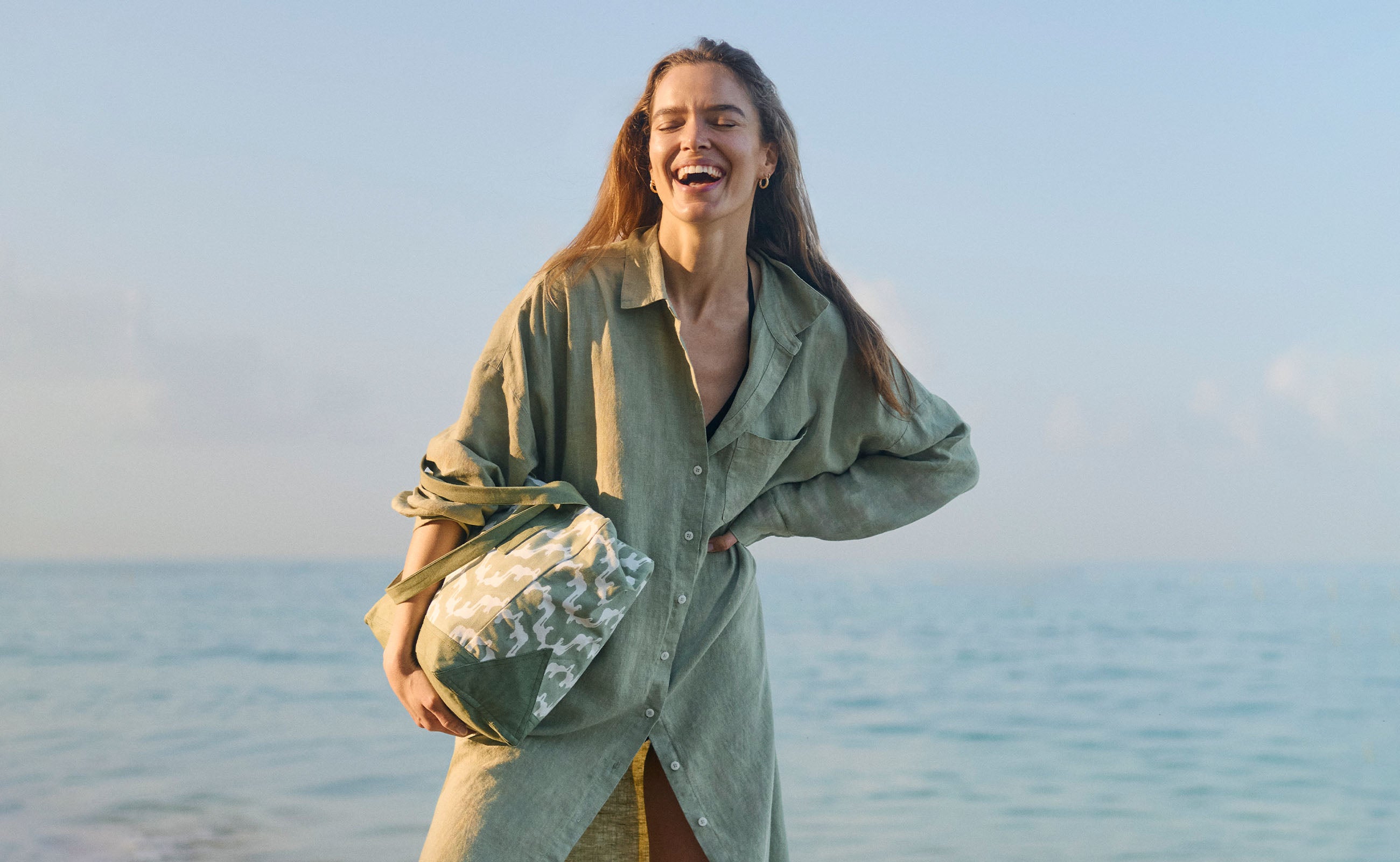 Woman holding a bag by the ocean with a clear blue sky