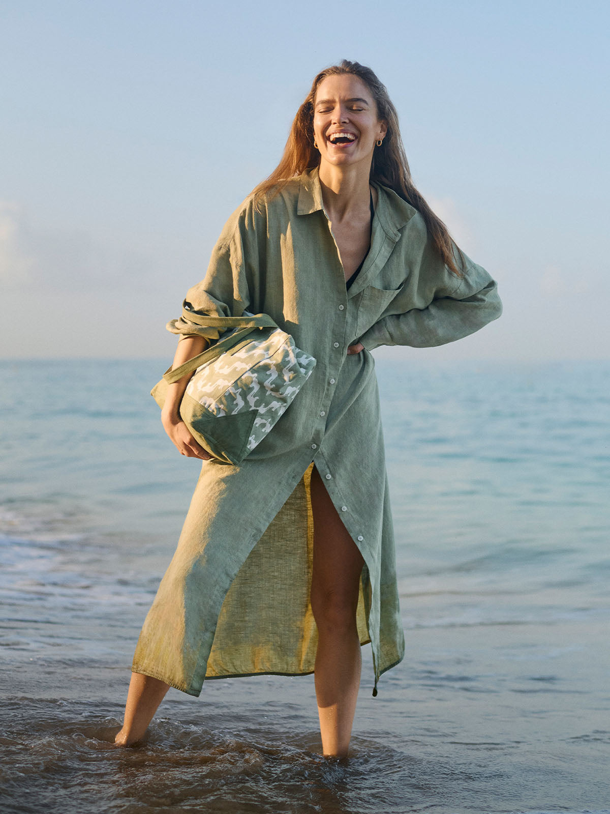 Woman in a green dress standing on a beach with ocean in the background