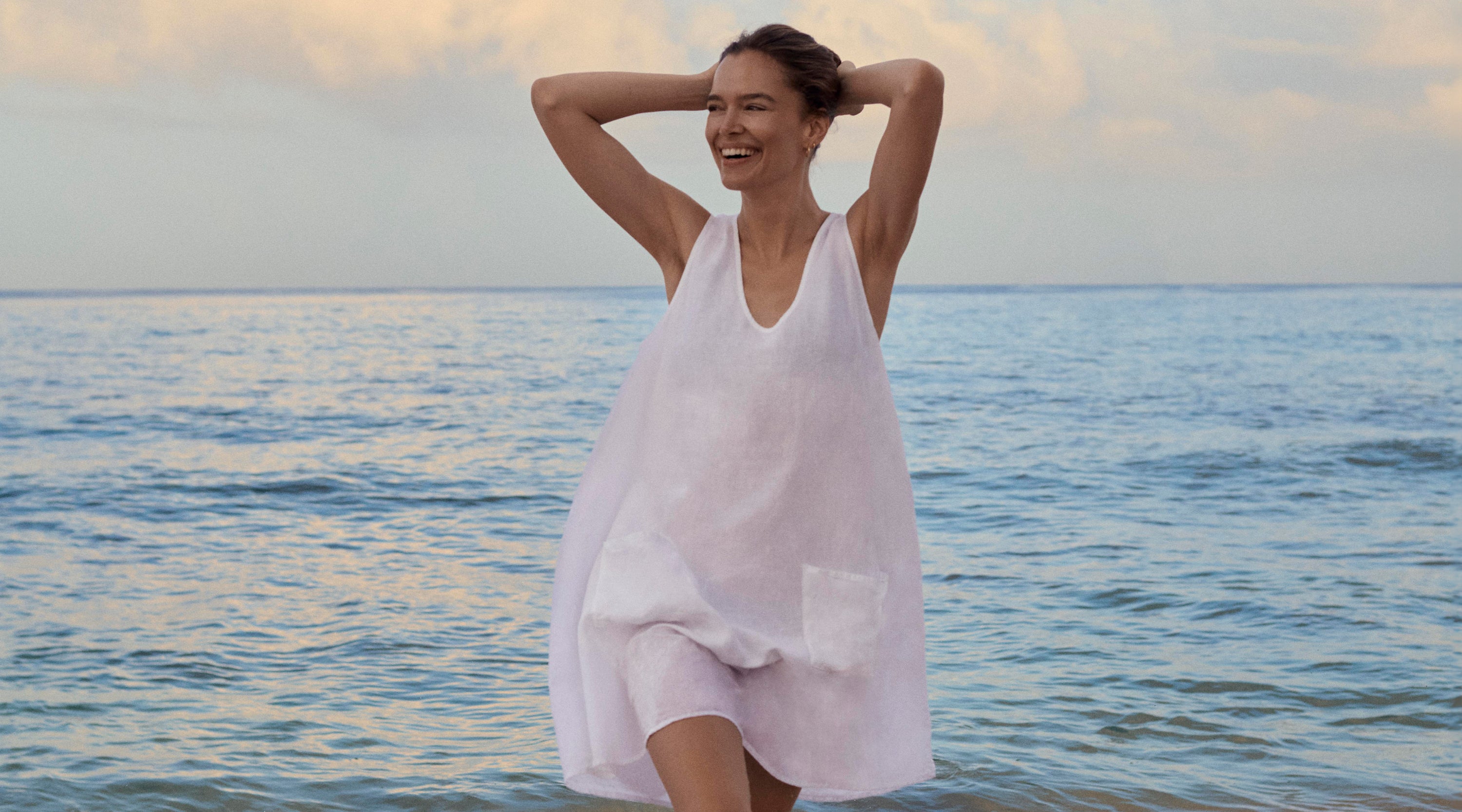 Women wears a white resort wear dress while standing in the ocean