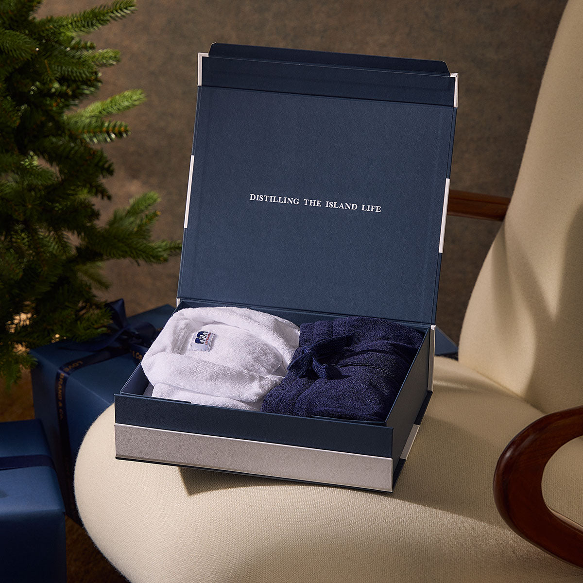 Open blue gift box with terry towelling items inside on a table next to a Christmas tree.