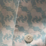 Close-up of Men's 60 & Still Roaring Abaco Linen Shirt featuring white lion print on a sky-blue background with a white button.