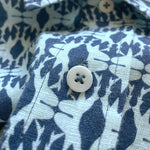 Close-up view of the Boys Shark Sanctuary Abaco Linen Shirt, featuring a white button and a pattern inspired by shark fins and silhouettes in shades of blue.