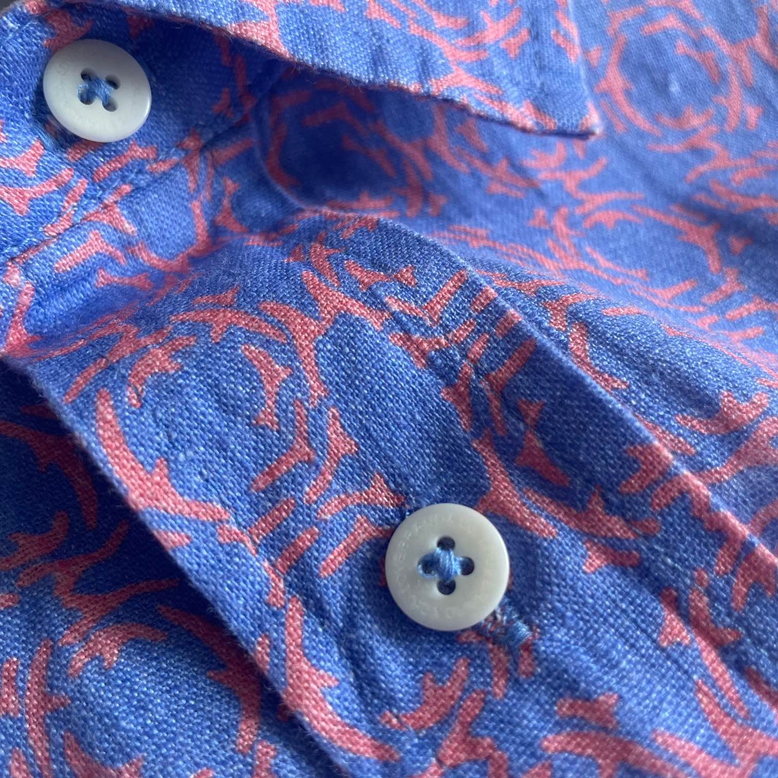 Close-up of Men's Omotion Manjack Linen Shirt with coral reef inspired geometric print in shades of blue and pink, featuring white buttons.