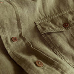 Close-up of the Men's Olive Green Andros Hemp Shirt showcasing the durable 100% organic hemp fabric, pleated double chest pocket, and signature corozo nut buttons.