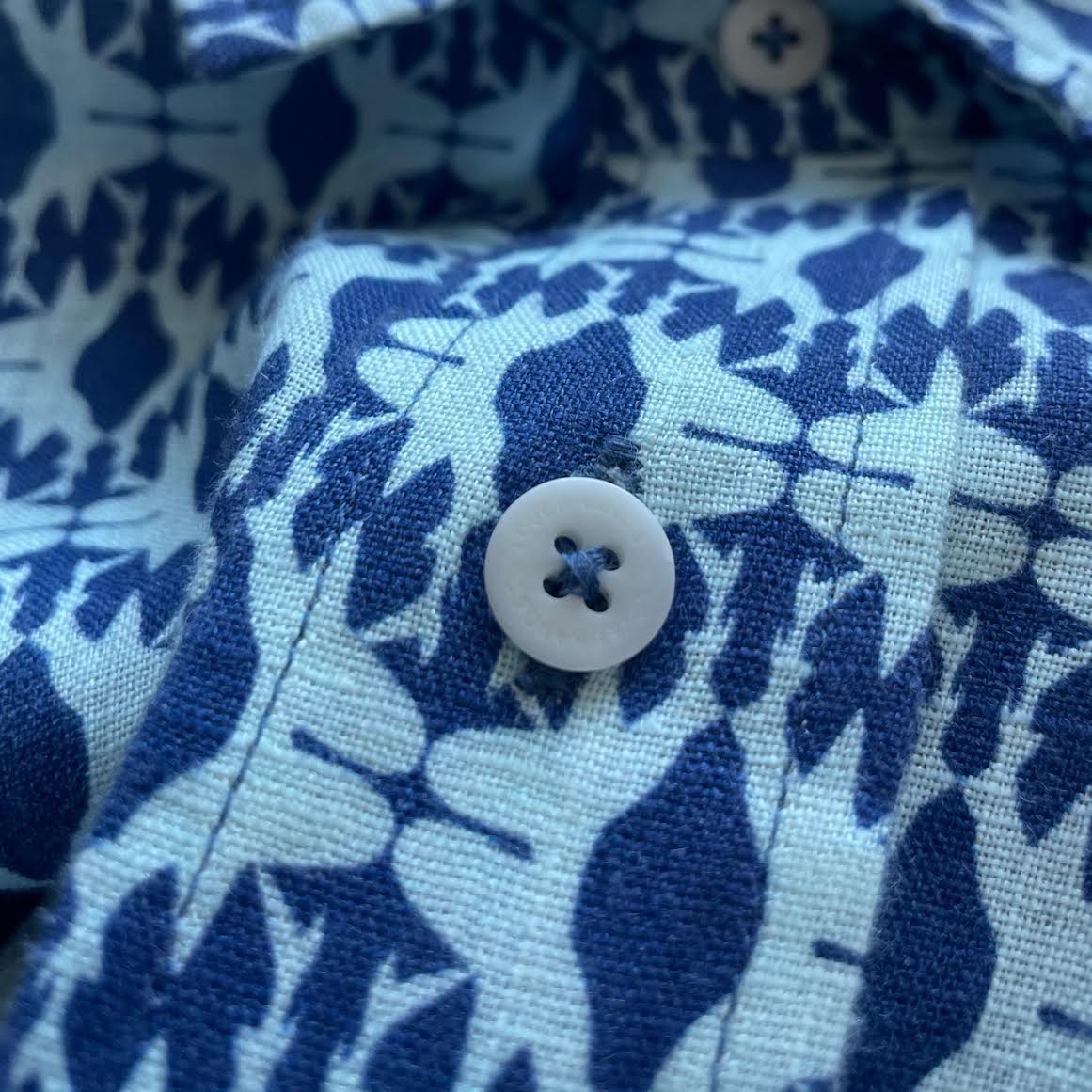 Close-up of the button and fabric pattern of the Men's Shark Sanctuary Abaco Linen Shirt, showcasing the intricate design of shark fin silhouettes in shades of blue.