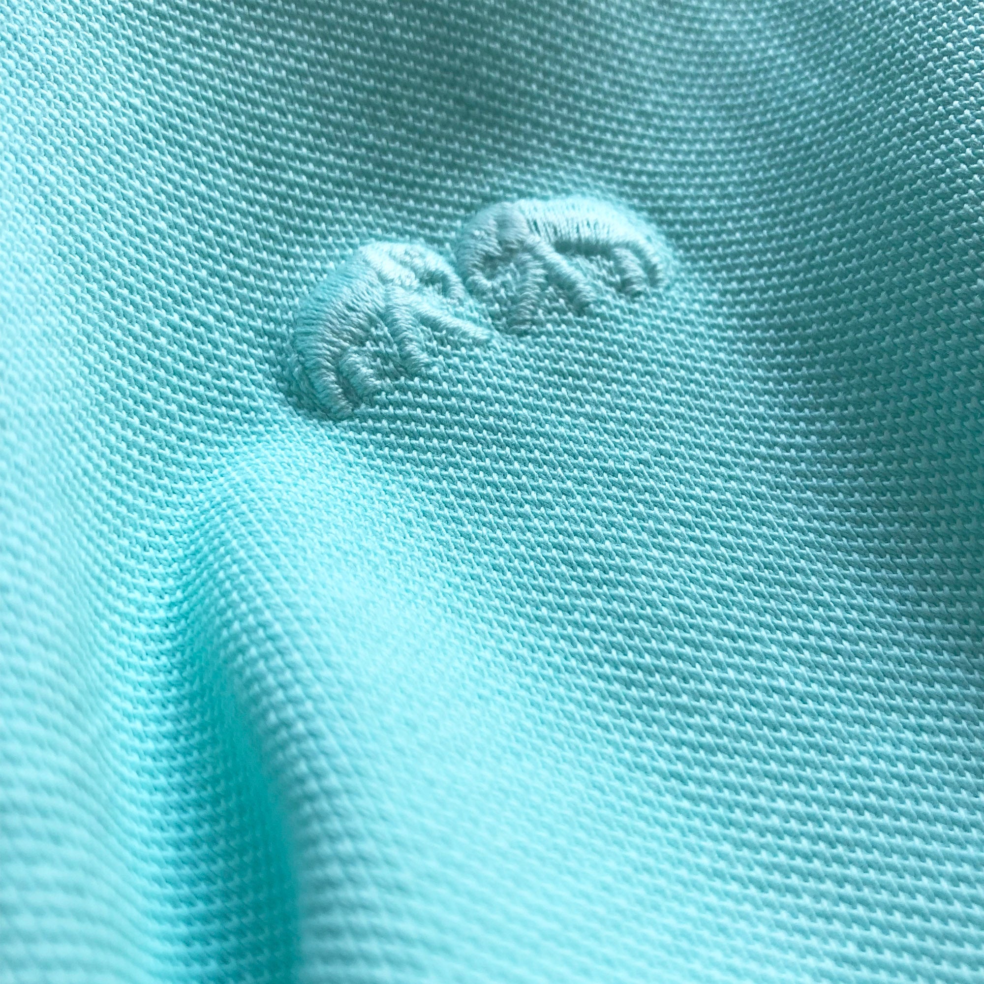 Close-up of the Men's Cay Green Pensacola Polo Shirt fabric and embroidered logo, inspired by the aqua hues of Bahamian seas.