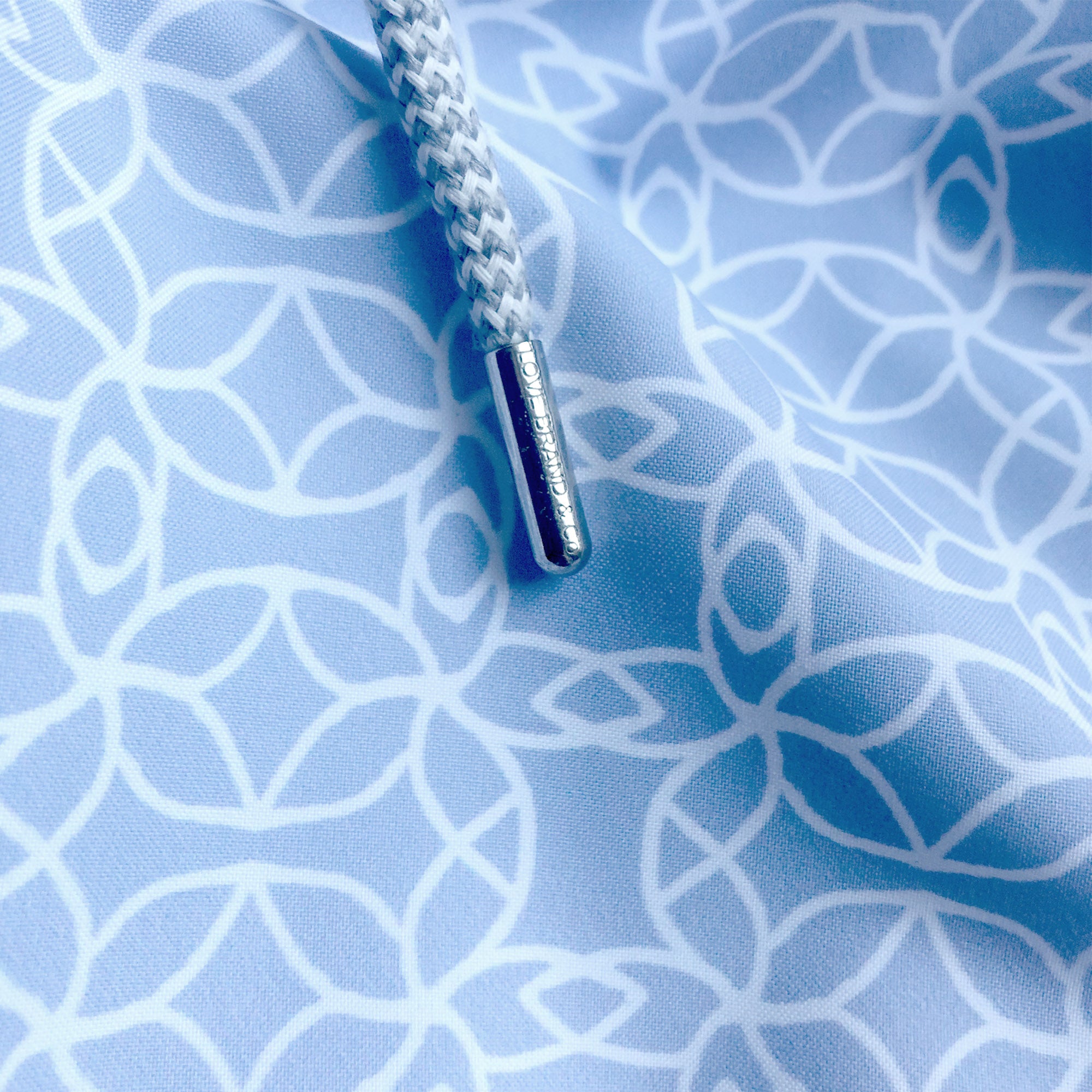 Close-up of the Men's Regeneration Staniel Swim Shorts fabric with a light blue geometric pattern and a braided drawstring.