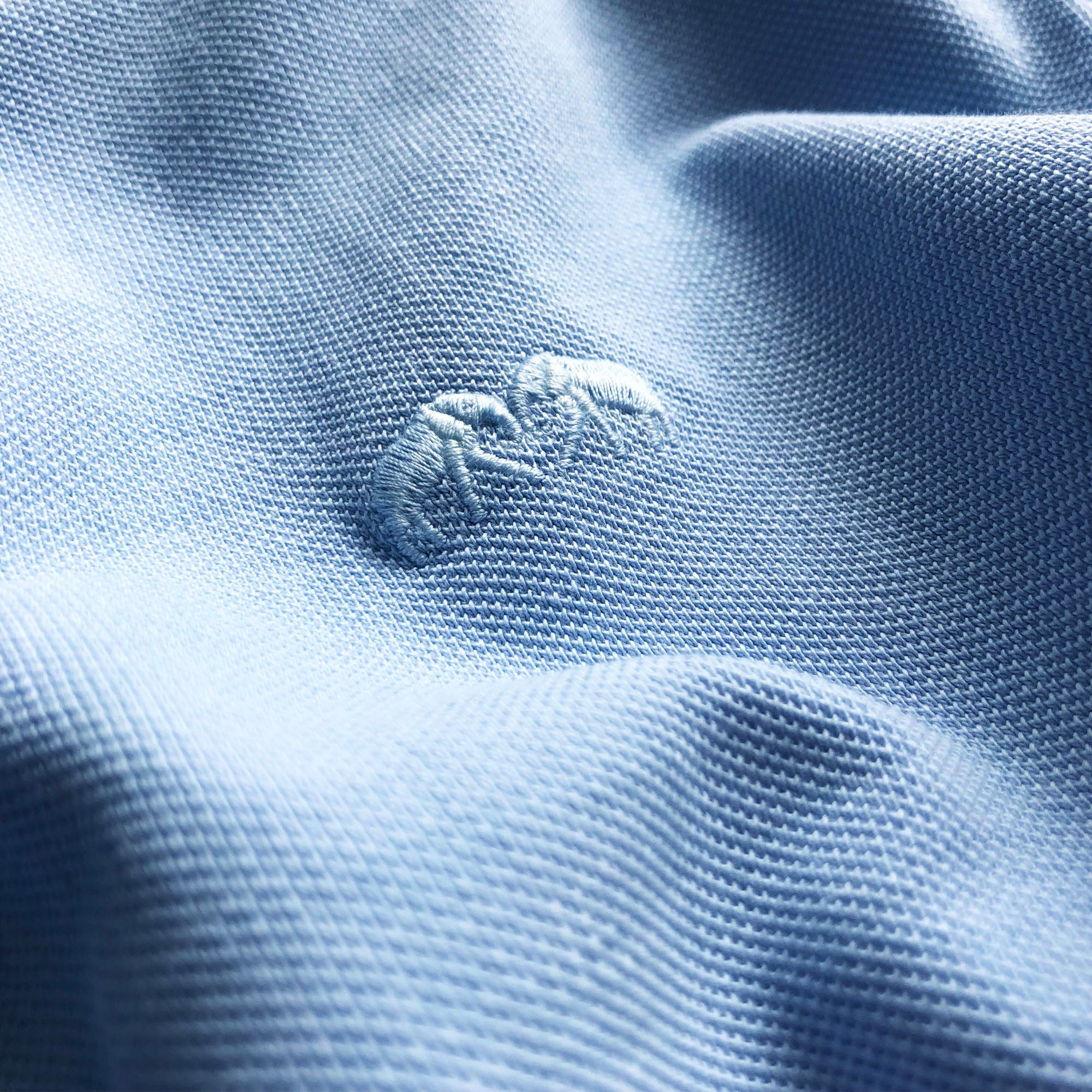 Men's Sky Blue Pensacola Polo Shirt fabric with embossed logo detail.